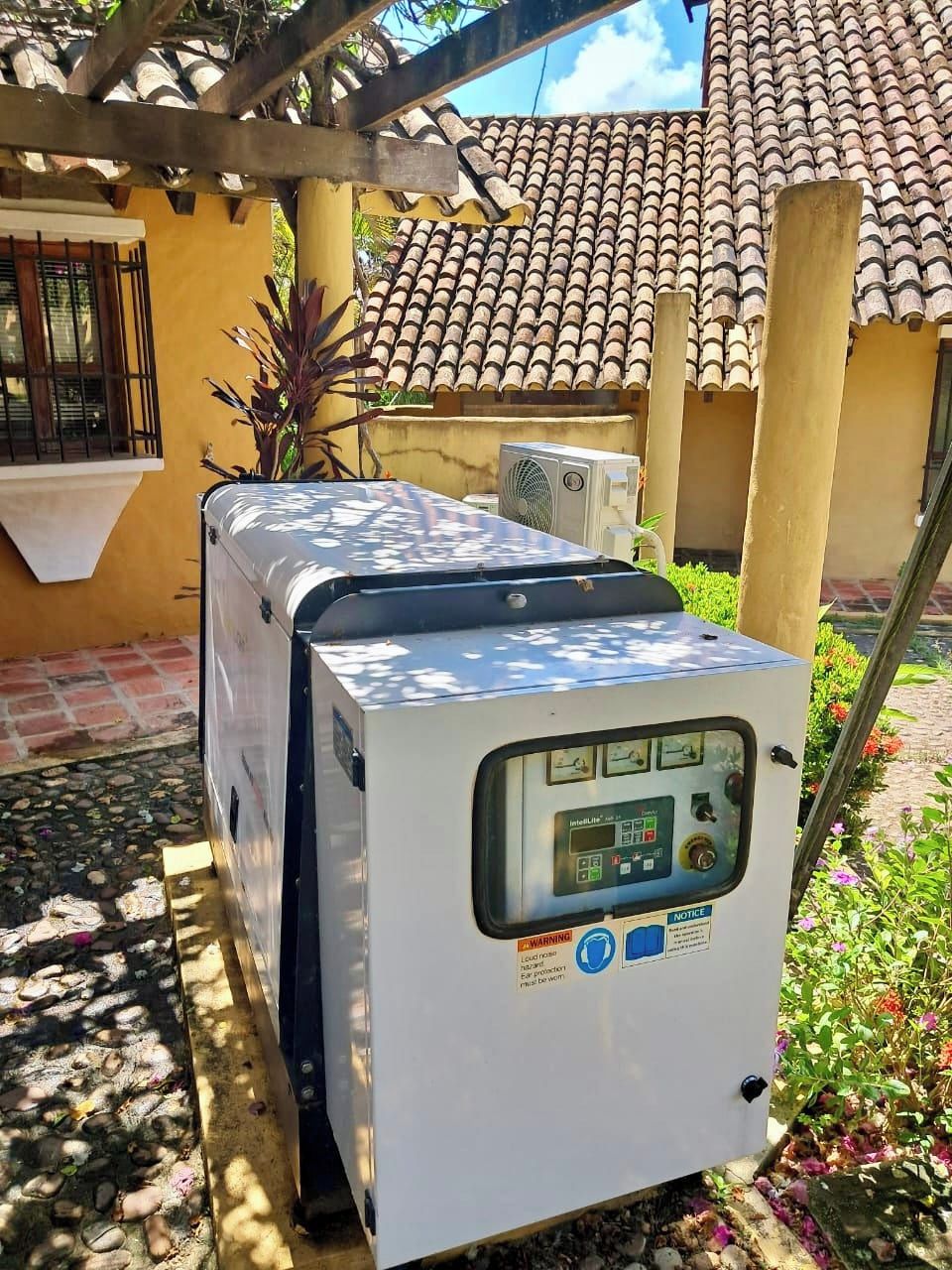 Un climatiseur portatif blanc, doté d’un panneau de commande, est placé à l’extérieur, sur une terrasse dotée d’un toit en tuiles et agrémentée de plantes.