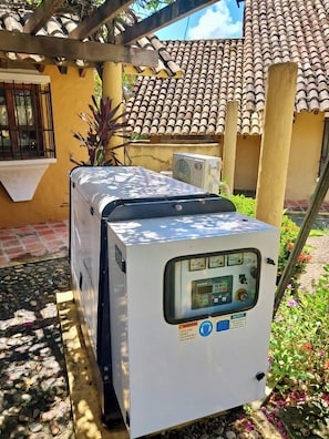 Un climatiseur portatif blanc, doté d’un panneau de commande, est placé à l’extérieur, sur une terrasse dotée d’un toit en tuiles et agrémentée de plantes.