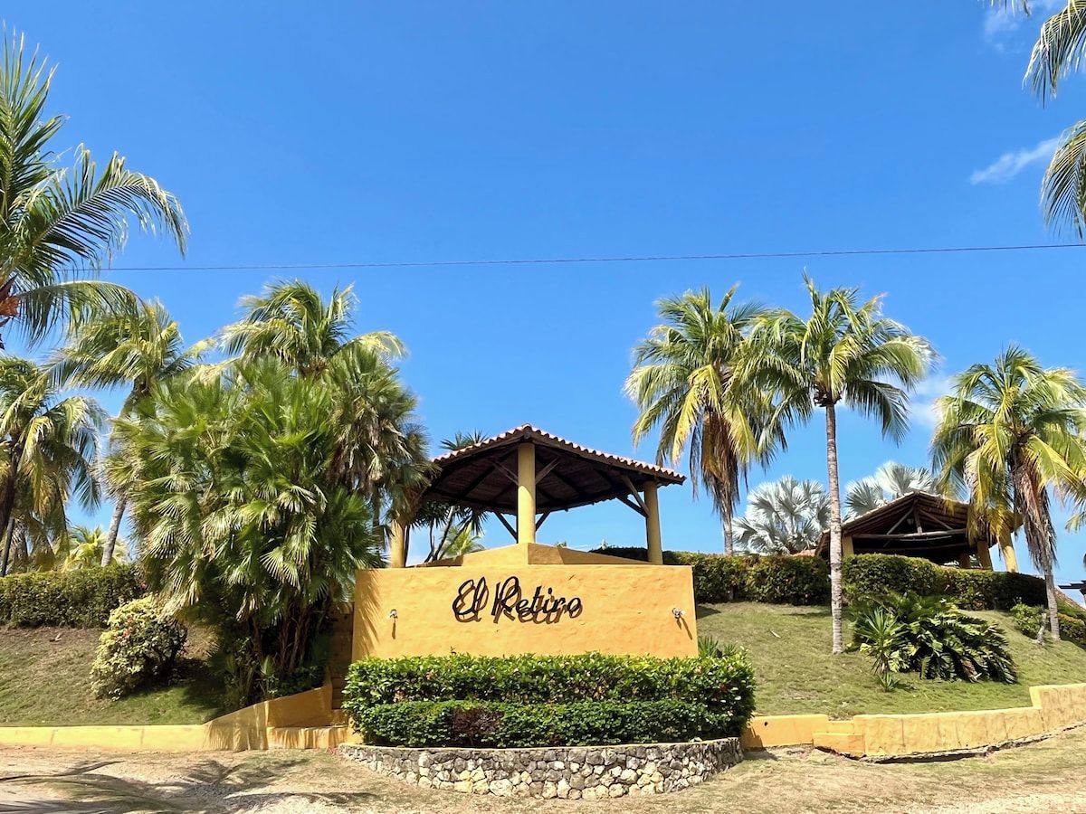 A sign with 'El Retiro' written on it, surrounded by palm trees and a clear blue sky.