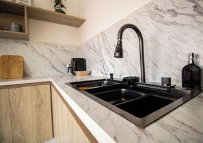 A kitchen with a black faucet, a wooden cutting board, and a marble backsplash.