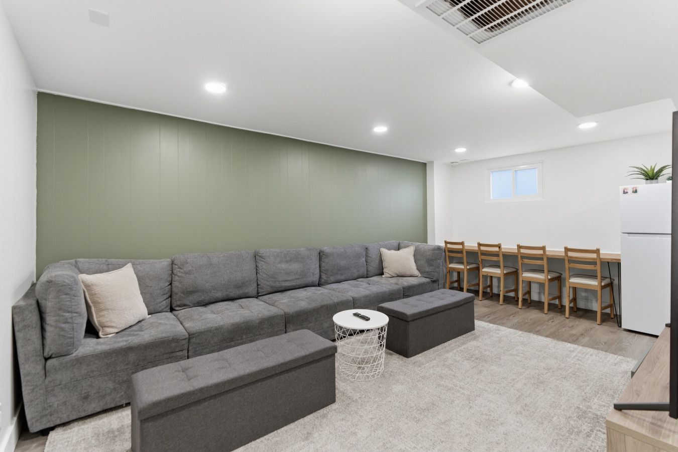 A modern living room with a grey sectional sofa, a small round coffee table, and a dining area with wooden chairs and a white table.