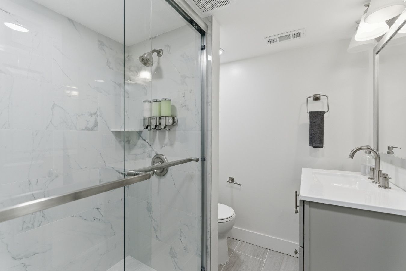 Un baño moderno con cabina de ducha de vidrio, inodoro y lavabo con espejo.