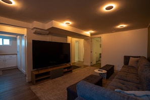 Una sala de estar moderna con televisor de pantalla plana, un sofá, una mesa de centro e iluminación empotrada en el techo.