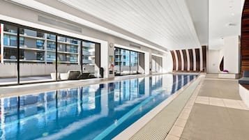 Una piscina interior con agua cristalina, suelo de baldosas y diseño arquitectónico moderno con amplias ventanas y techos altos.