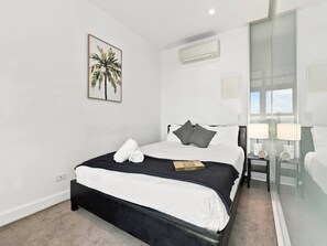 Een moderne hotelkamer met een groot bed, een klein nachtkastje, een bijzettafeltje, een glazen scheidingswand en een airconditioning.