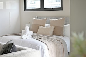 A modern bedroom with a large bed, a bedside table, and a window. - Elegant Corner 1BR on Bree St with City & Mountain Views & AC (Cape Town)