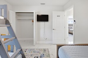 A bedroom with a bed, a TV mounted on the wall, a closet, and a door leading to another room. - Waterfront Escape Heated
Pool Kayaks & Boat Lift (Apollo Beach)