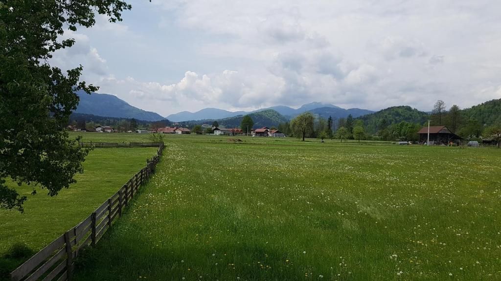 A rural landscape with a fenced field, houses, and mountains in the background.