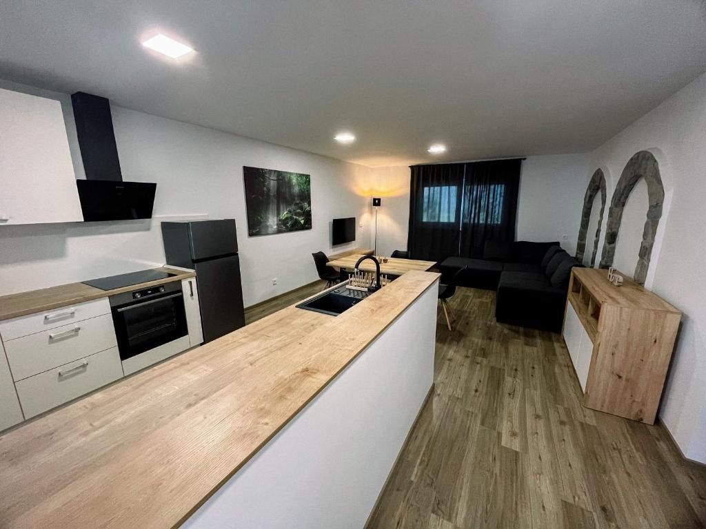 A modern kitchen with a central island, built-in oven, and a dining area with a black sofa and wooden sideboard.
