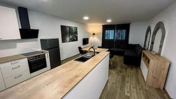 A modern kitchen with a central island, built-in oven, and a dining area with a black sofa and wooden sideboard.