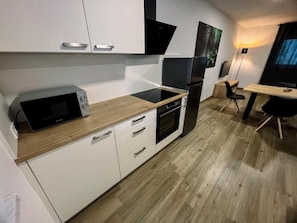 Una cocina compacta con gabinetes blancos, microondas, horno y refrigerador.