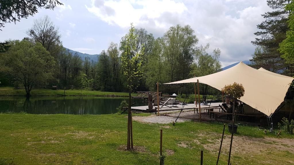 A lakeside campsite with a table and chairs, a large canopy, and a dock extending into the water.