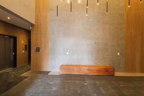 A modern lobby with a wooden bench, a textured wall, and an elevator. - Nex One Faria Lima NR (São Paulo)