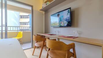 Un espace repas moderne avec une longue table, des chaises et un téléviseur à écran plat fixé au mur.