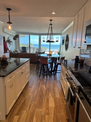 A modern kitchen with wooden flooring, a central island, and a view of the ocean. - Toes-in-the-Sand - Oceanfront Views - New Smyrna Beach (New Smyrna Beach)