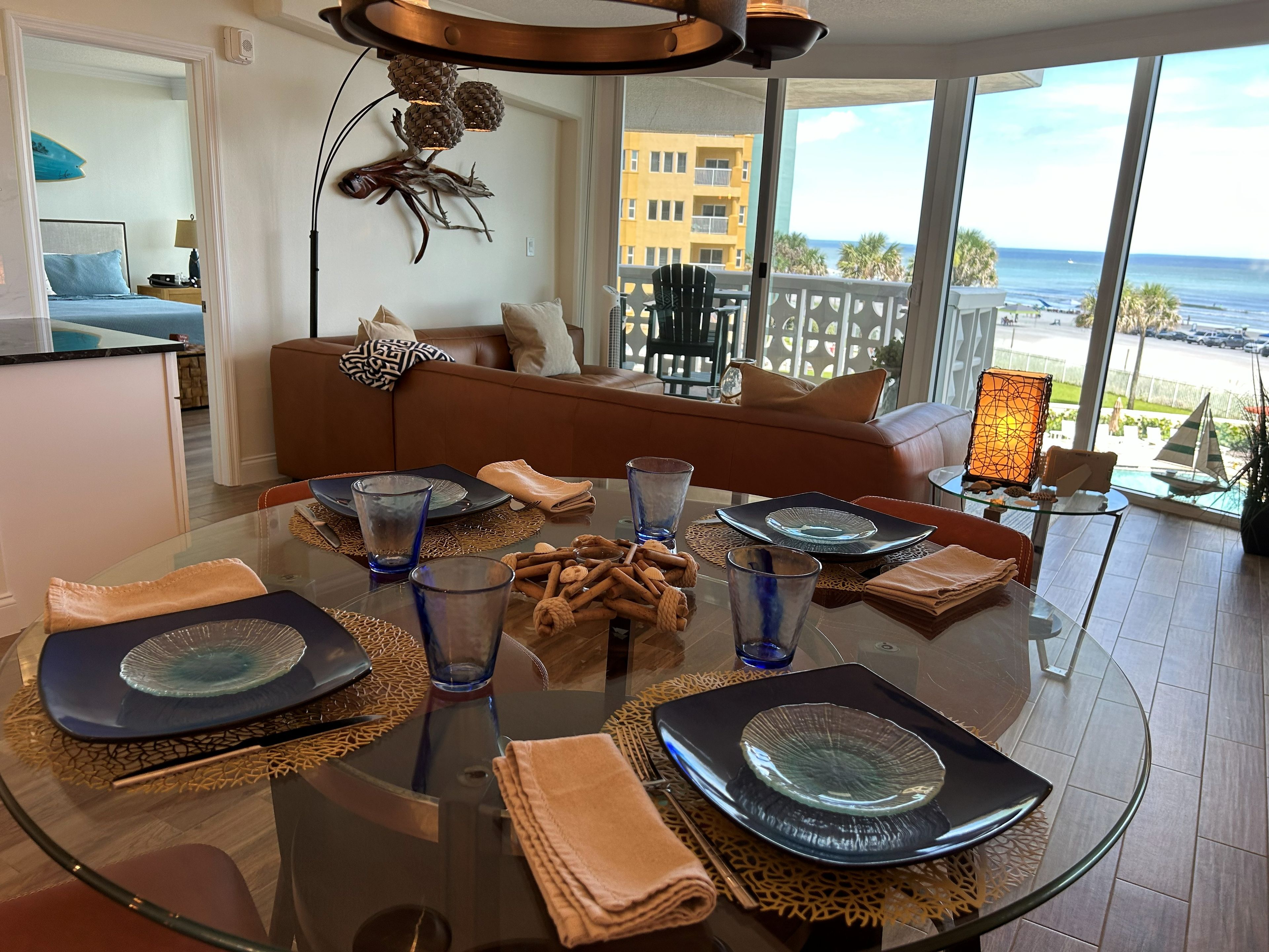 Un comedor moderno con una mesa de vidrio, platos azules y negros, y vista al océano.