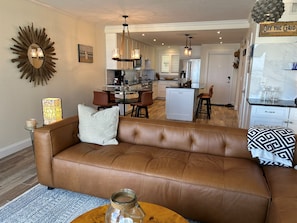 A living room with a brown leather sofa, a coffee table, and a decorative mirror. - Toes-in-the-Sand - Oceanfront Views - New Smyrna Beach (New Smyrna Beach)