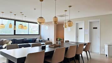 Uma sala de jantar moderna com uma mesa comprida e várias cadeiras, um sofá e iluminação pendente.