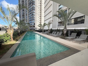 A swimming pool with lounge chairs, surrounded by palm trees and modern buildings. - Wonder Ipiranga By Housi (São Paulo)