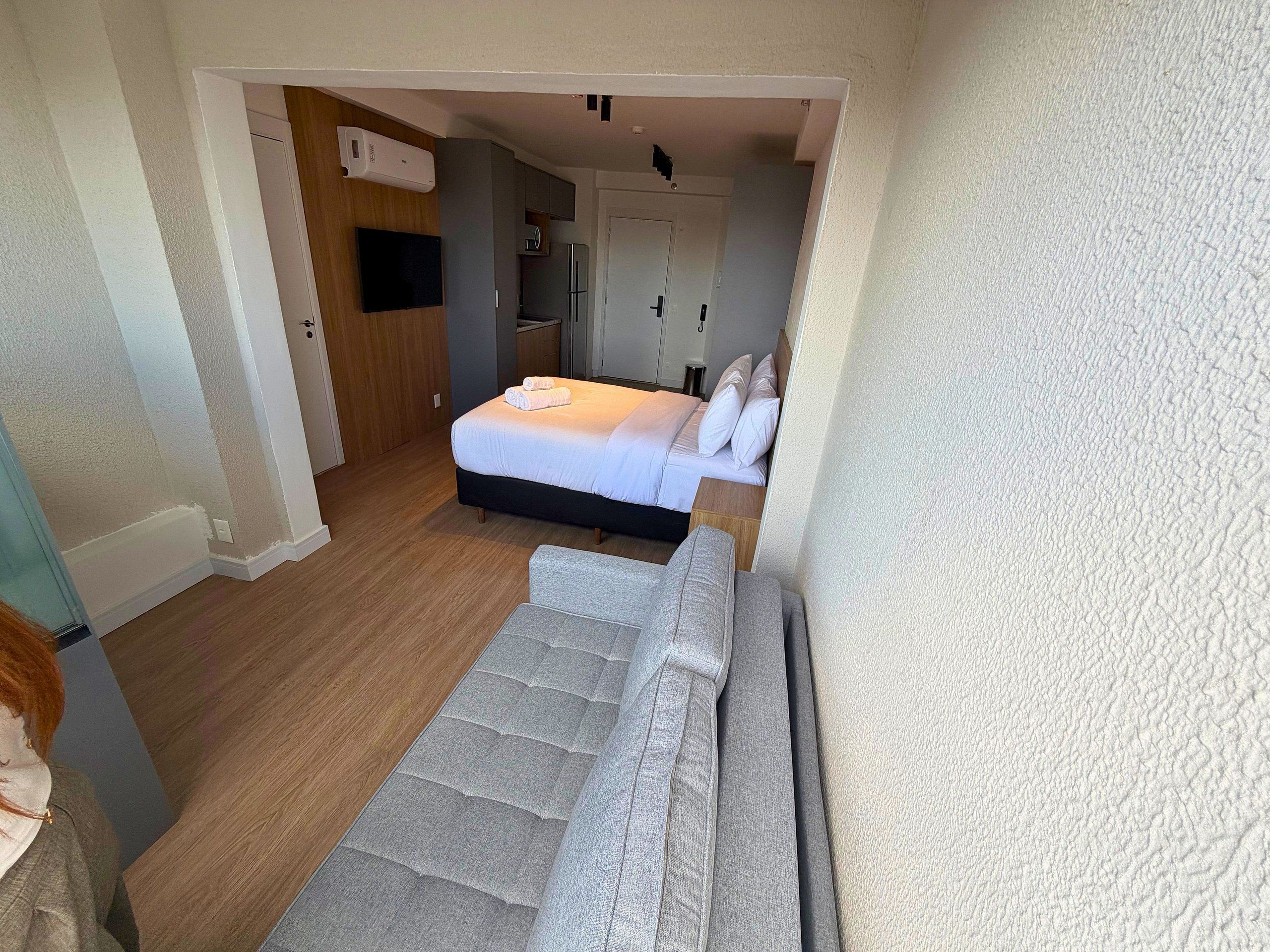 Quarto de hotel com cama, uma pequena cozinha e banheiro.