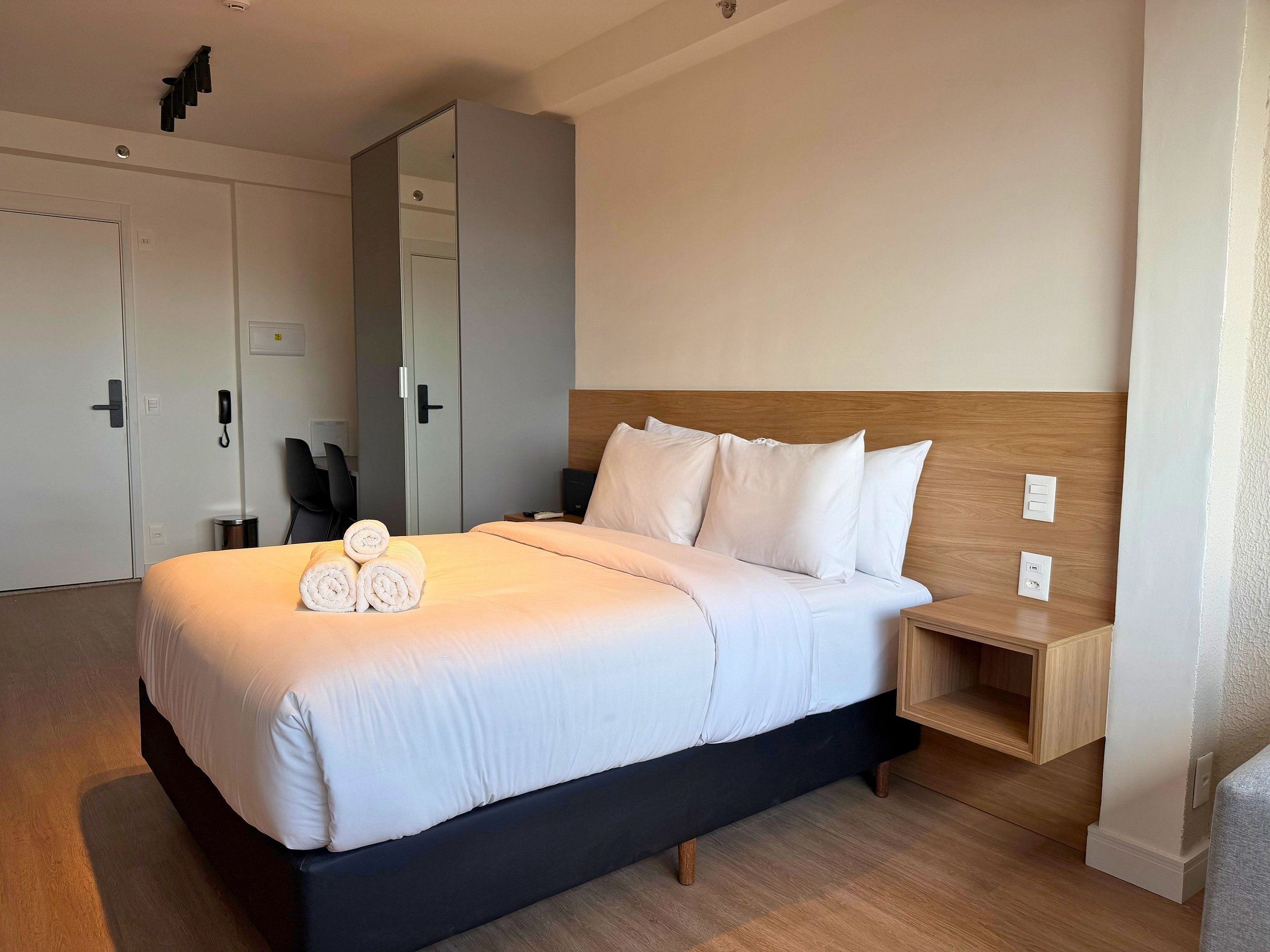 A hotel room with a bed, a bedside table, a mirror, a wardrobe, and a chair.