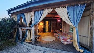 A wooden porch with a round rug, a sofa, and curtains.
