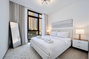 A modern hotel room with a large bed, a bedside table with a lamp, a mirror, and a window with a city view. - Elegant 1BR Retreat in Palace Residences | Creek (Dubai)
