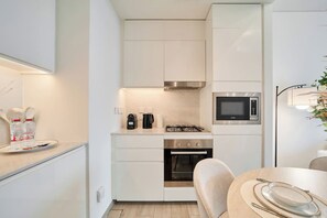 A compact kitchen with white cabinetry, a microwave, a stove, and a dining area with a table set for two. - Elegant 1BR Retreat in Palace Residences | Creek (Dubai)