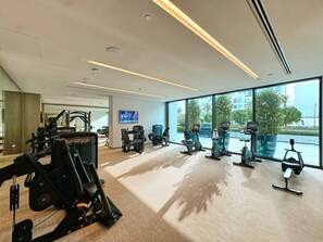 Une salle de sport équipée de divers appareils d’exercice, dotée de grandes fenêtres et d’un écran de télévision.