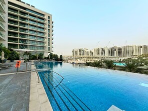 A swimming pool with a clear view of a high-rise building in the background. - Chic 1BR Escape in Palace Residences | Creek (Dubai)