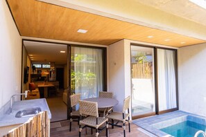 Une terrasse extérieure moderne dotée d’une piscine, d’un espace repas et de portes-fenêtres coulissantes donnant sur une cuisine et un salon.