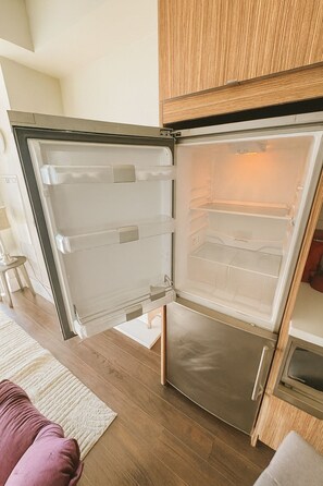 A modern kitchen with a stainless steel refrigerator, wooden cabinets, and a wooden floor. - New · Monthly 1BR Condo by CN Tower & PATH (Toronto)