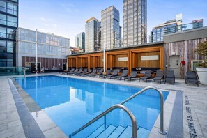 A swimming pool with lounge chairs and a view of modern buildings. - New · Monthly 1BR Condo by CN Tower & PATH (Toronto)