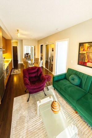 Una sala de estar moderna con un sofá verde, un sillón rojo y una mesa de centro de cristal.
