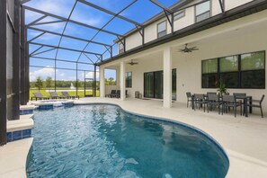 A modern indoor swimming pool with clear blue water, surrounded by a covered patio area with outdoor seating and a view of a green landscape. - Paradiso Grande 15br Suites, Pool & Themed Rooms (Orlando)
