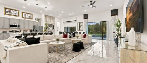 A spacious living room with a sofa, coffee table, and ottomans, a kitchen with modern appliances, and a large window offering a view.