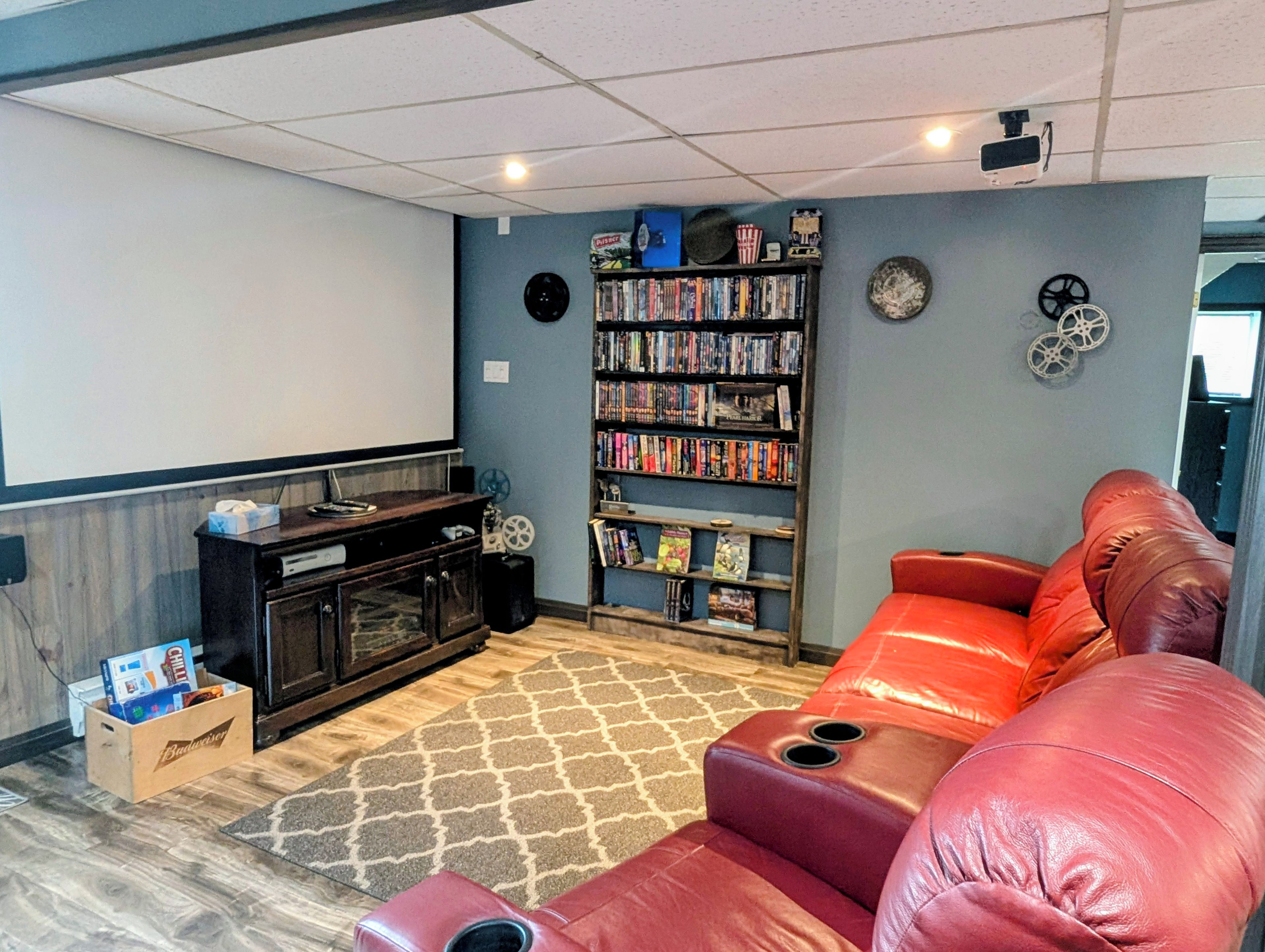A home theater room with a large screen, a bookshelf, a red leather couch, and a wooden entertainment unit.