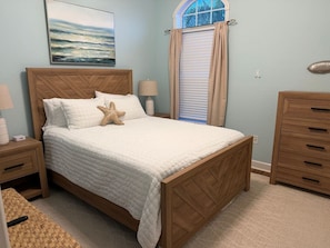 A bedroom with a wooden bed, a starfish pillow, a lamp, and a window with curtains. - Salty Serenity | Your Hernando Beach Escape (Hernando Beach)