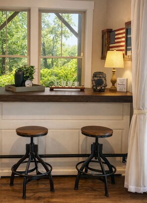 A kitchen with two bar stools, a window with a view of greenery, a tray with a clock and glasses, and a lamp with a sign. - New Listing: Modern Mountain Farmhouse with Views (Union Mills)