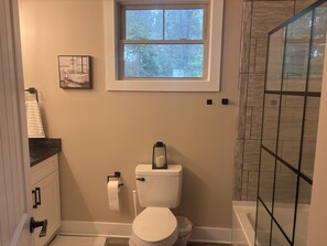 Un baño con inodoro, ventana, ducha y toallero.
