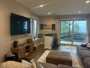 A modern living room with a flat-screen TV, wooden cabinets, a sofa, and a sliding glass door leading to a patio. - New Listing: Modern Mountain Farmhouse with Views (Union Mills)