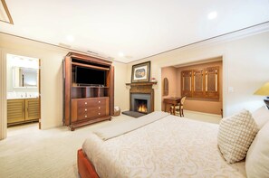 Een slaapkamer met een bed, een dressoir, een televisie, een open haard en een spiegel.