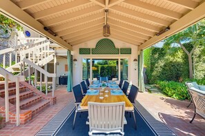 Ein überdachter Essbereich im Freien mit einem Holztisch und -stühlen, einer Treppe und Blick auf einen üppigen Garten.