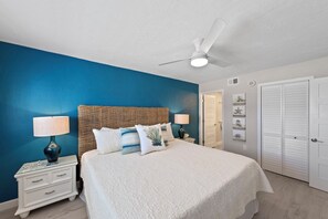A bedroom with a bed, nightstands, a ceiling fan, and a door. - Sunset 602-Perfect Beachfront Escape (Fort Myers Beach)
