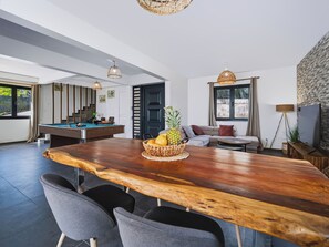 A modern living room with a wooden dining table, grey chairs, a pool table, and a sofa. - Villa Infini Blue—A Family Getaway with a Pool, Hot Tub, Pool Table, and Kids' Games (Les Trois-Îlets)