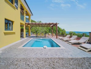 A pool area with a pergola, lounge chairs, and a view of the sea. - Villa Infini Blue—A Family Getaway with a Pool, Hot Tub, Pool Table, and Kids' Games (Les Trois-Îlets)