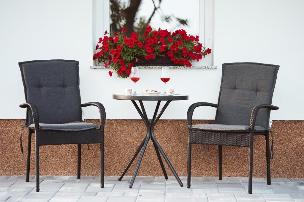 Dos sillas con asientos y respaldos acolchados, una mesita redonda con un pilar central y una ventana con un arreglo floral rojo.