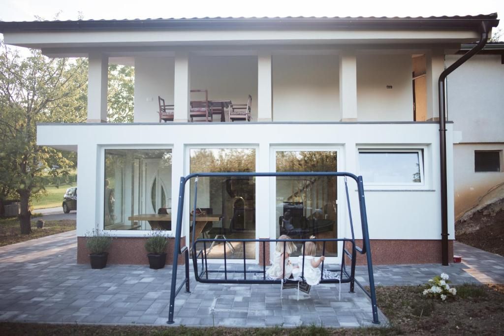 A modern two-story house with a balcony, large windows, and a swing set in the front yard.