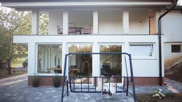 A modern two-story house with a balcony, large windows, and a swing set in the front yard.