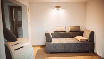A room with a grey sofa, a white chair, and a wooden floor.